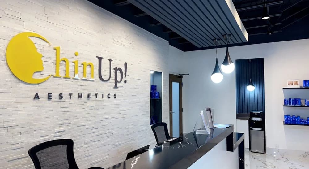 Chin Up Aesthetics Decatur lobby — branded stone wall with the gold moon-face logo